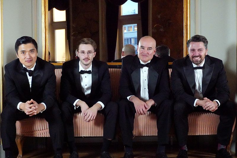 Quartett nebeneinander sitzend im holzgetäfelten Salon